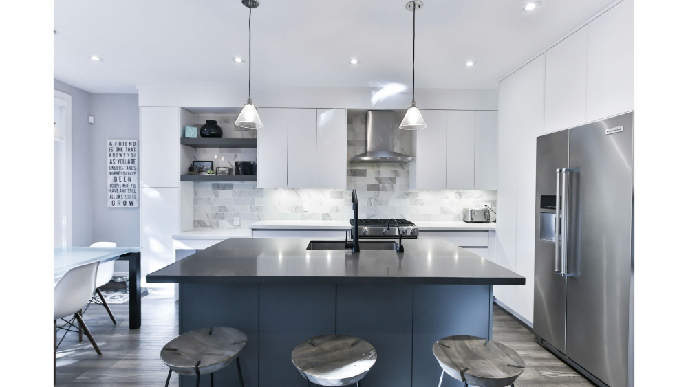 Contemporary Kitchen With A Gray Island, White Cabinets, Marble Backsplash, Pendant Lighting, And Stainless Steel Appliances In A Sleek, Minimal Design.